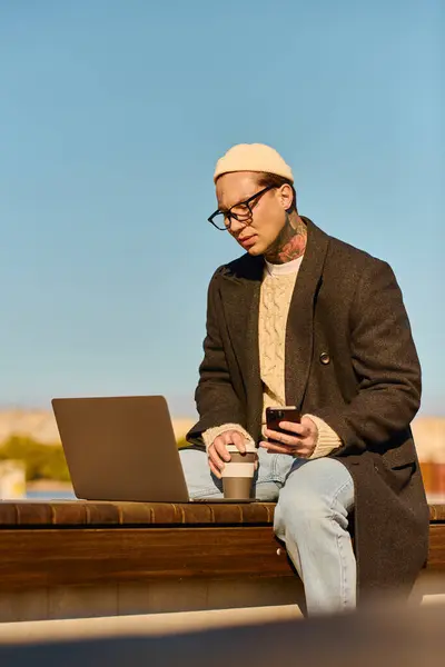 Handsome man in a chic outfit focuses on his laptop while sipping coffee in a sunny location. — Stock Photo