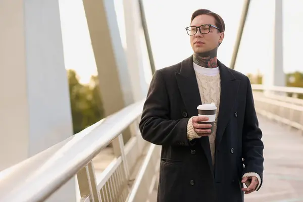 Elegante hombre toma un paseo pausado en un día brillante, saboreando su café con confianza y estilo. - foto de stock