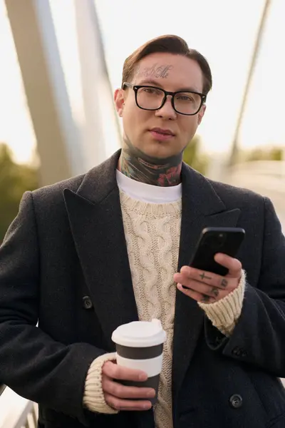 Bello uomo in abito alla moda posa con caffè e smartphone sullo sfondo contemporaneo. — Foto stock