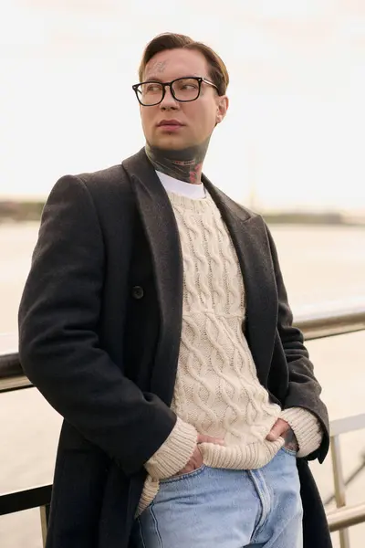 Young man with tattoos shows off modern fashion while enjoying a beautiful day by the water. — Stock Photo