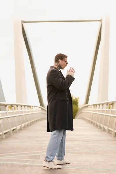 Ein junger Mann mit Tätowierungen posiert elegant auf einer glatten Brücke und präsentiert zeitgenössische Mode. — Stockfoto