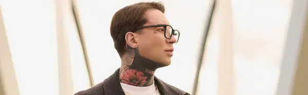 A stylish man displays his tattoos by modern architecture. — Stock Photo