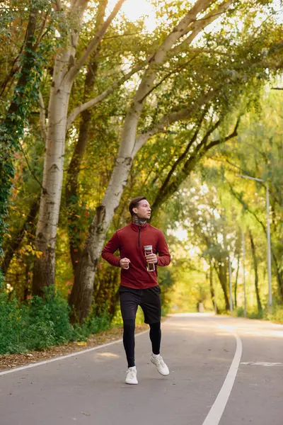 Bello uomo in un abito chic corre lungo un percorso alberato, abbracciando la calda luce solare autunnale. — Foto stock