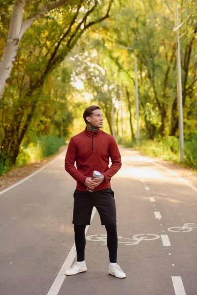 A young man in athletic wear poses confidently on a tree lined path, showing off his style. — Stock Photo