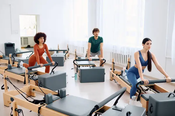 Three focused individuals practice pilates using reformers in a bright and spacious studio. — Stock Photo