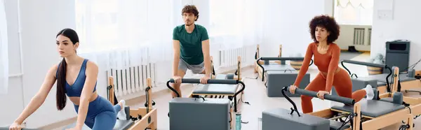 Three participants focus on their exercises in a bright, modern pilates studio environment. — Stock Photo