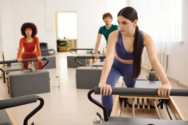 Three individuals practice pilates with reformers in a bright, airy studio during morning hours. — Stock Photo