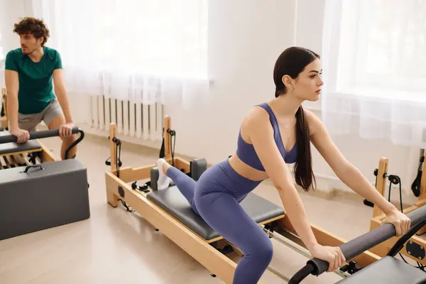 Zwei Personen absolvieren gezielte Pilates-Workouts mit Reformer-Geräten in einem gut beleuchteten Studio. — Stockfoto
