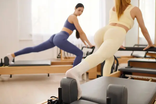 Two women engage in pilates exercises, focusing on strength and flexibility inside a bright studio. — Stock Photo