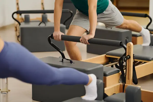 Two individuals practice pilates using specialized equipment in a well lit studio space. — Stock Photo
