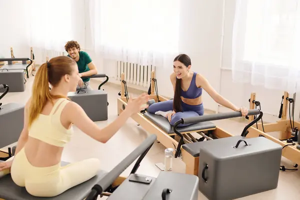 Two women chat lively while doing pilates on reformers in a bright studio. — Stock Photo
