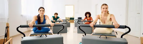 Los participantes se centran atentamente mientras practican pilates con equipo de reformador en un amplio estudio. - foto de stock
