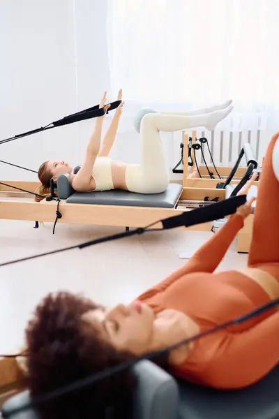 Duas mulheres fazem pilates desafiadores em reformadores em um estúdio iluminado pelo sol, com foco em força e equilíbrio. — Fotografia de Stock