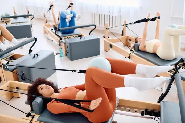 Grupo de individuos entusiastas practicando pilates en un estudio bien iluminado usando máquinas reformadoras - foto de stock