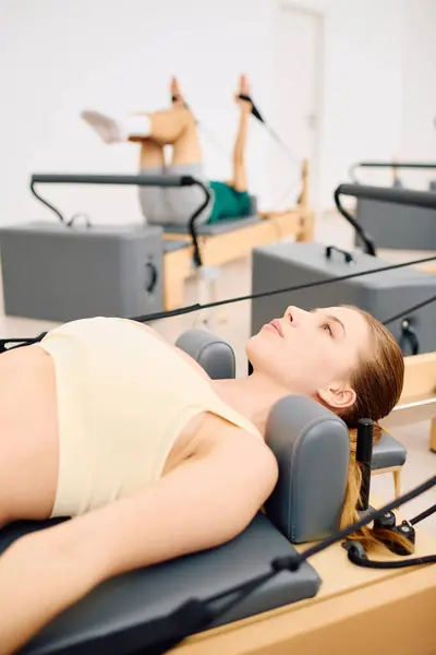 Una donna fa pilates su un riformatore mentre un altro partecipante si estende nelle vicinanze. — Foto stock