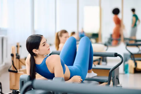 Une jeune femme utilise un réformateur dans une séance d'entraînement pilates dynamique pour stimuler sa force de base. — Photo de stock