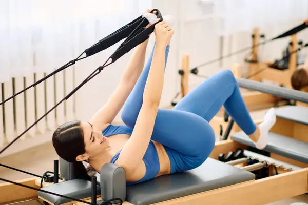 Engaging in a pilates session, a woman uses equipment to enhance her strength and flexibility. — Stock Photo