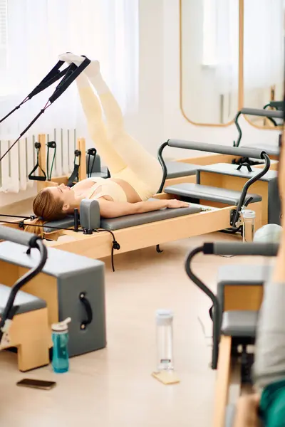 Una persona esegue un allenamento di pilates utilizzando un riformatore in uno studio pieno di luce, migliorando la forma fisica. — Foto stock
