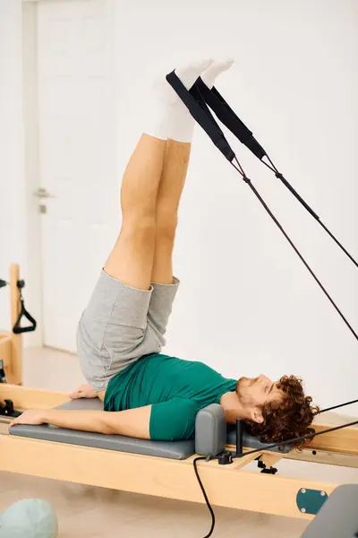 A man engages in a pilates workout using a reformer, focusing on leg lifts for core stability. — Stock Photo