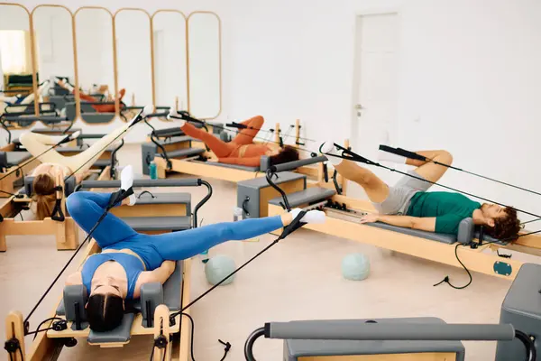 Grupo de indivíduos realizando exercícios de pilates sincronizados em um ambiente de estúdio bem iluminado — Fotografia de Stock