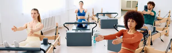 Participantes em roupas coloridas se concentram em sua rotina de pilates usando reformadores em um estúdio ensolarado. — Fotografia de Stock
