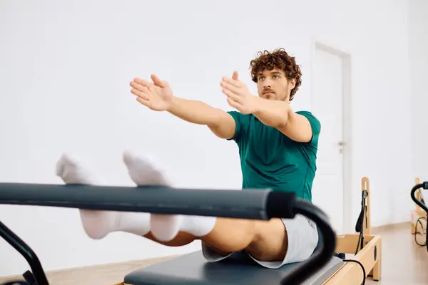 A man practices controlled movements on a reformer in a bright, spacious pilates studio. — Stock Photo