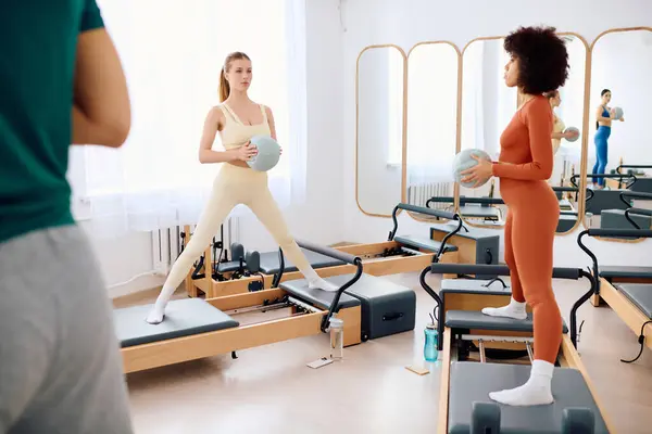 Dos individuos practican pilates con accesorios en un ambiente amplio y luminoso. - foto de stock