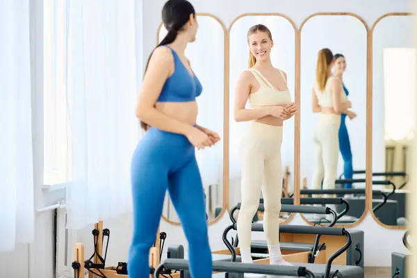 Women exchange smiles and encouragement while practicing pilates in a well lit studio setting. — Stock Photo