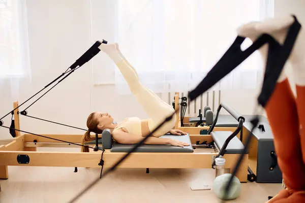 Un individuo dedicado ejecuta levantamientos de piernas en un reformador, inmerso en un ambiente de estudio calmante. — Stock Photo