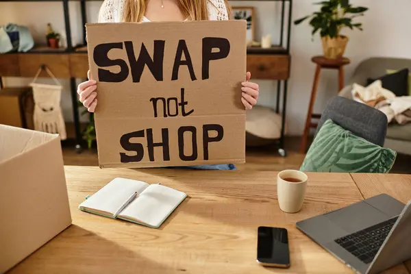 Young woman holds a sign promoting clothes swapping while sorting her donations. — Stock Photo