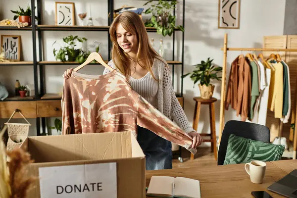 Joyful young woman sorts clothes for donation, embracing a sustainable lifestyle at home. — Stock Photo