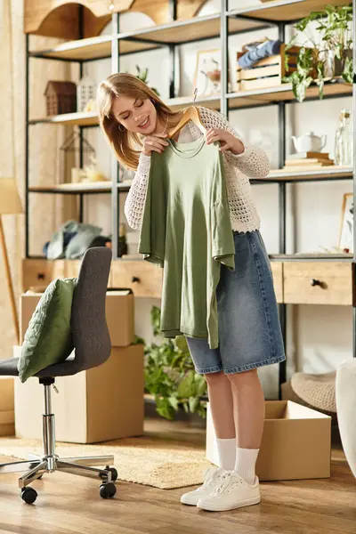 Young woman smiling while sorting clothes for donation in her stylish, eco-friendly home. — Stock Photo