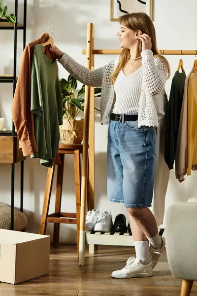 A young woman sorts through her clothes, choosing items for donation in a stylish room setting. — Stock Photo