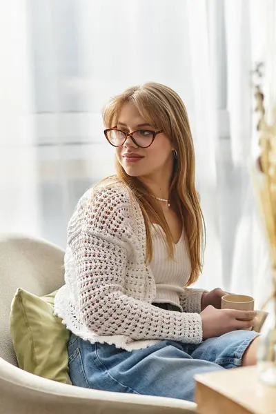 A young woman enjoying a warm beverage while relaxing at home, surrounded by light. — Stock Photo