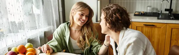 Young couple sits at a modern kitchen table, sharing smiles and a light snack in their cozy home. — Stock Photo