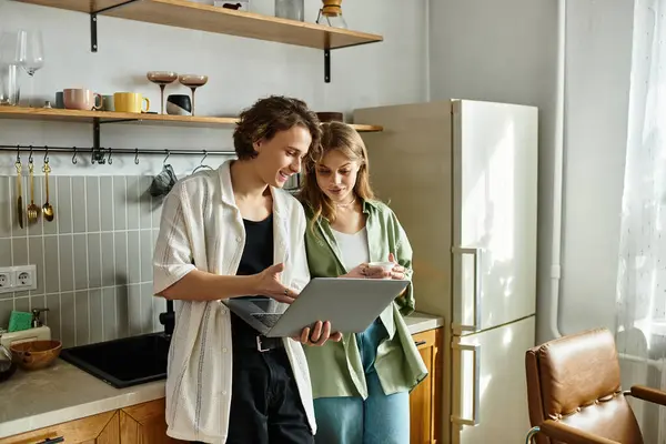 A loving couple stands close in their modern kitchen, sharing smiles while looking at a laptop. — Stock Photo