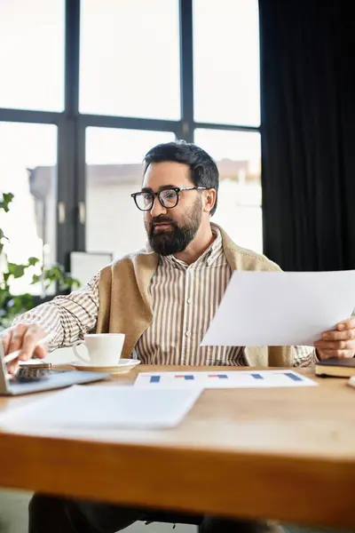 Un homme âgé passe en revue des documents avec une boisson chaude à une table en bois dans son espace de travail confortable. — Photo de stock