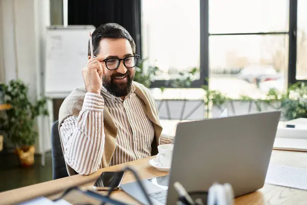 Handsome senior man smiles and holds a pencil while engaging with his laptop at work. — Stock Photo