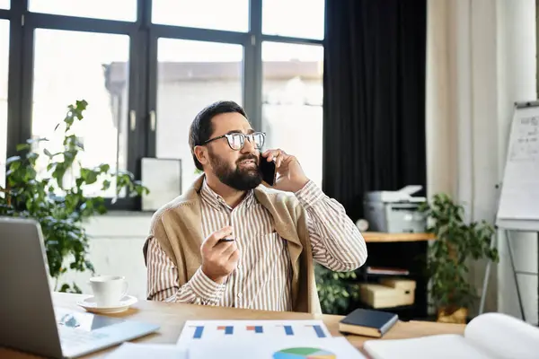 Elderly man with glasses enjoys a phone conversation while sitting at a desk surrounded by plants. — Stock Photo