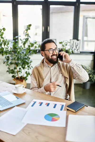 A charming elderly man smiles during a lively discussion at a wooden desk, surrounded by plants. — Stock Photo