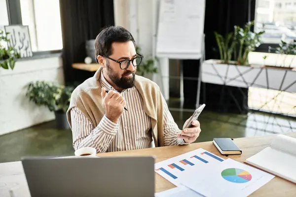 Handsome senior man sits at a desk, thoughtfully checking his device and pondering his projects. — Stock Photo