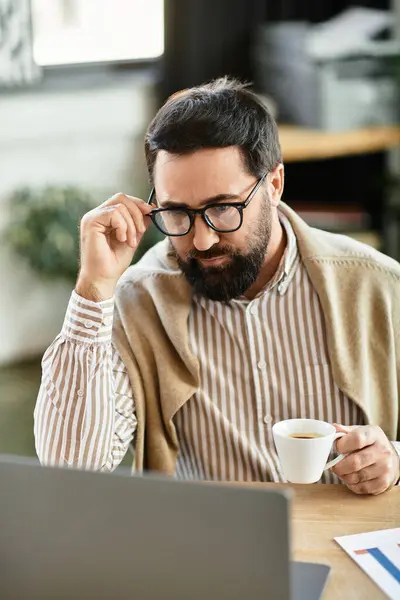 Senior man in casual clothes enjoys coffee while focused on his laptop in a relaxed setting. — Stock Photo