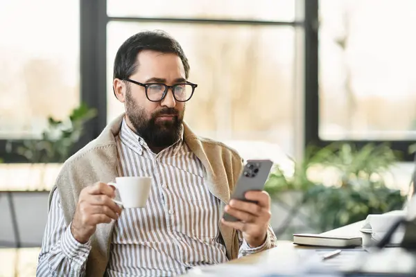 Handsome senior man in casual attire sips coffee and browses on his smartphone in a cozy cafe. — Stock Photo
