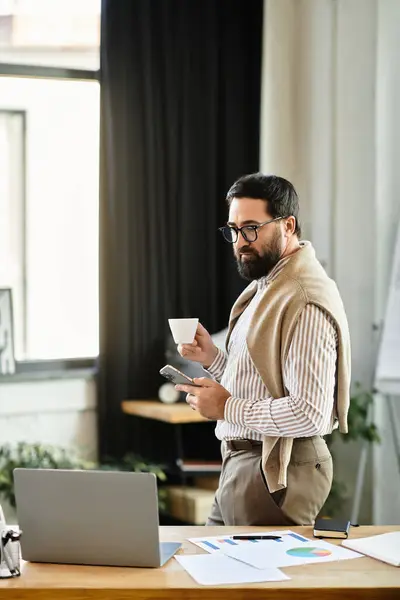 Handsome elderly man stands casually in a bright office, savoring coffee while checking his phone. — Stock Photo