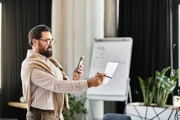 Homme âgé en tenue décontractée sourit alors qu'il vérifie les notes sur papier et un téléphone dans un espace de travail élégant. — Photo de stock