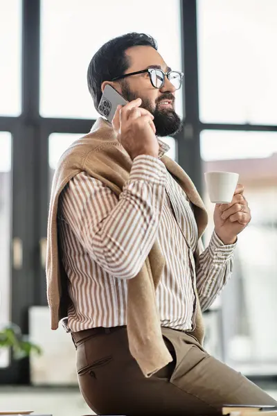 A stylish elderly man dressed casually talks on the phone while holding a cup, radiating charm. — Stock Photo