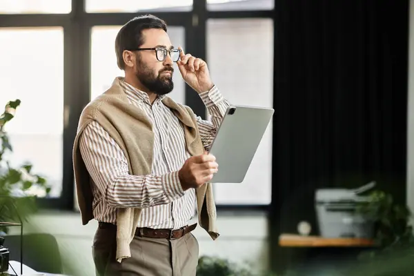 A senior man wearing casual attire thoughtfully examines a tablet while standing in a bright space. — Stock Photo