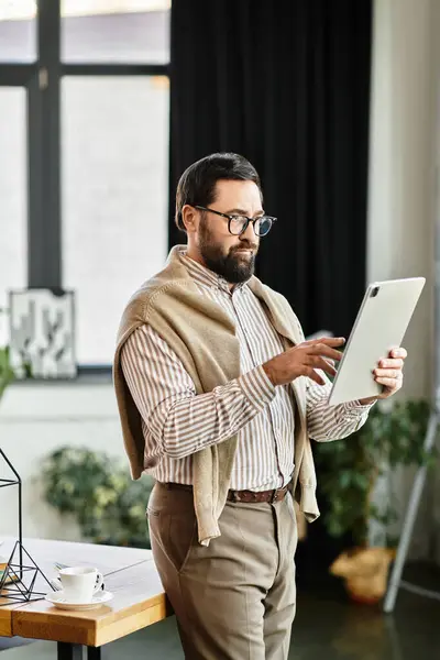 Ein gutaussehender älterer Mann in lässiger Kleidung interagiert mit einem Tablet in einem warmen, einladenden Raum. — Stockfoto