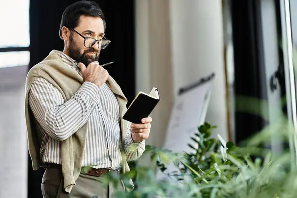 An attractive senior man thoughtfully writes in a notebook surrounded by lush greenery. — Stock Photo