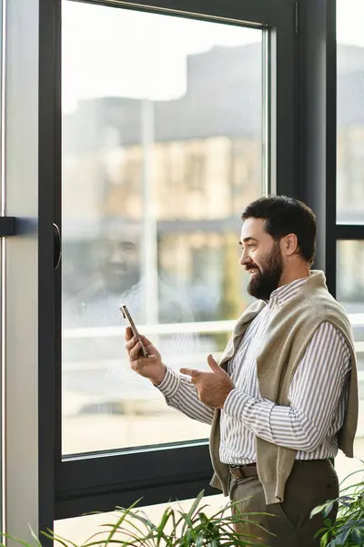 Elderly man smiles as he interacts with his smartphone near a bright window, exuding confidence. — Stock Photo